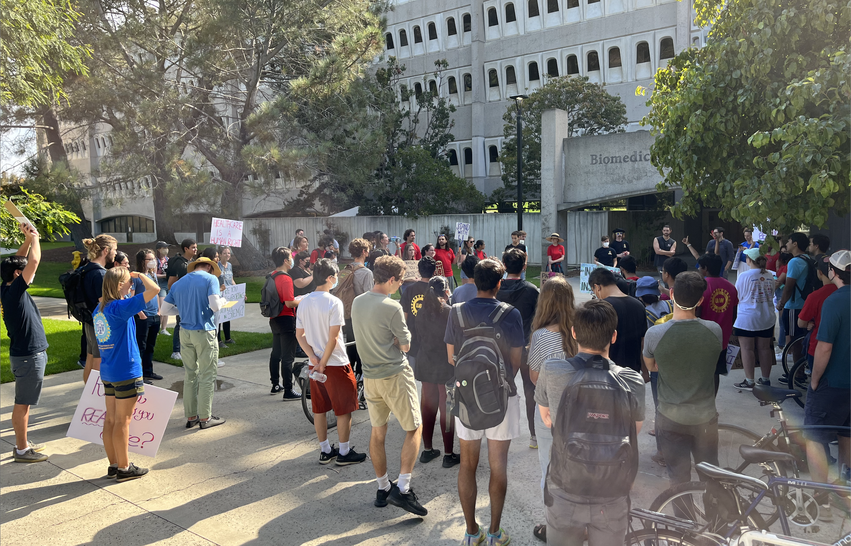 A crowd of dozens of workers holding picket signs and wearing UAW union shirts blocks the entrance to the Biomedical Sciences Building at UC San Diego